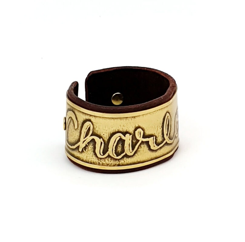 Artisanal brass and leather bracelet featuring a child's drawing of the name 'Charlotte' meticulously etched onto the brass surface.